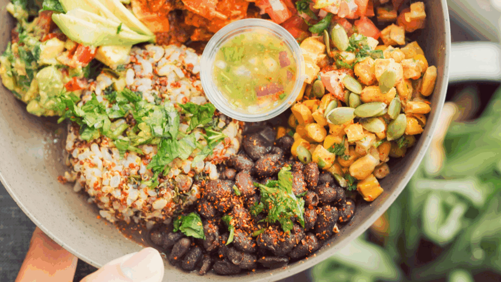 bowl of vegan Mexican food: beans, rice, corn, guacamole, tomato