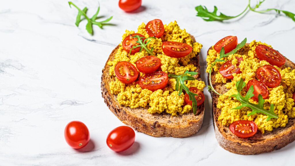 Delicious tofu scramble with tomatoes on toast on marble background
